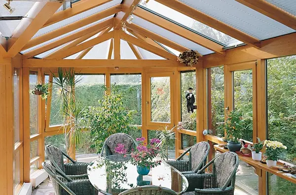 Heller Wintergarten aus Holz mit Glasdach, Pflanzen und gemütlicher Sitzgruppe im Grünen.