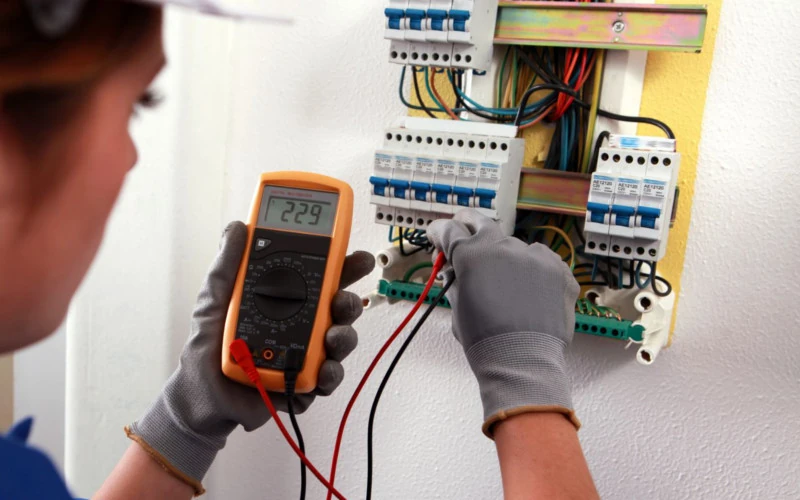 Elektriker misst Spannung im Sicherungskasten mit Multimeter und Prüfkabeln