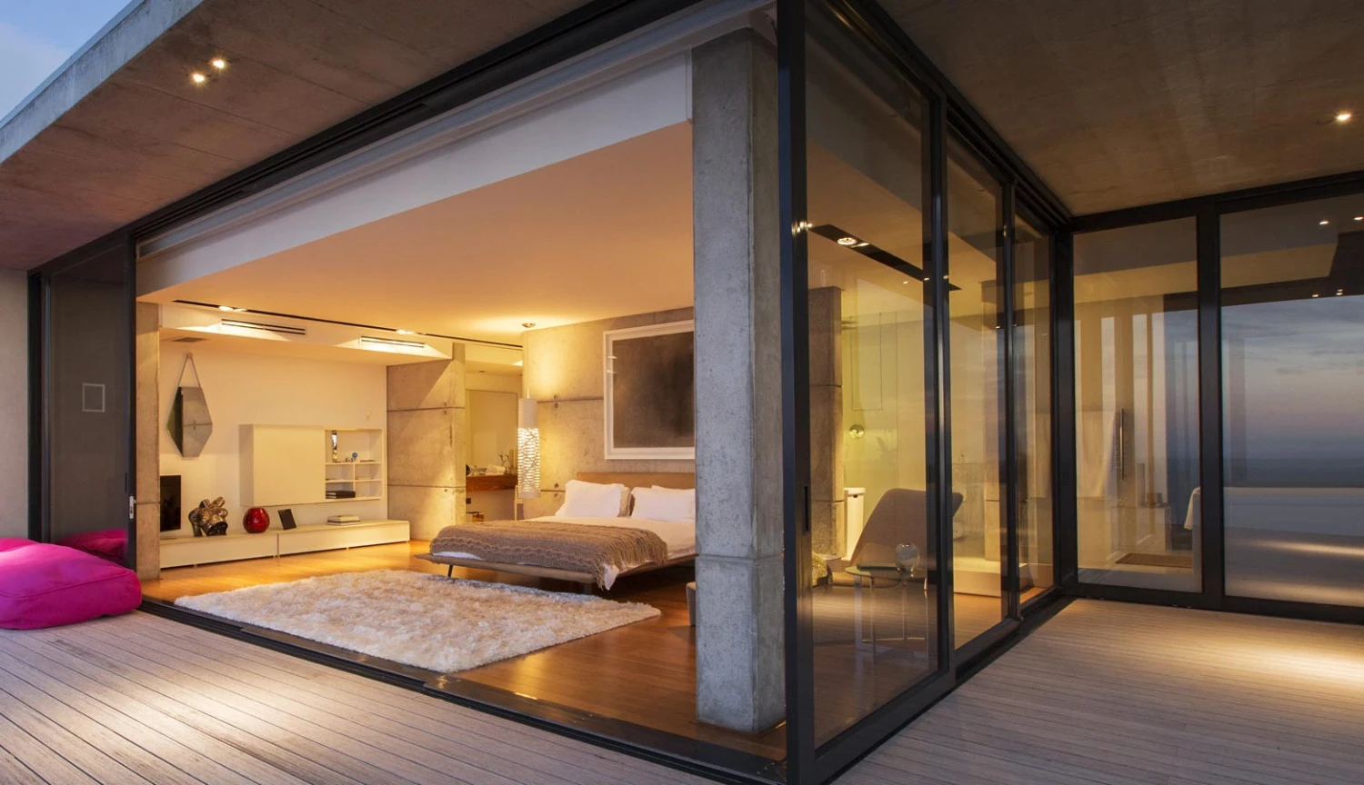Modernes Schlafzimmer mit Glasfront, Holzterrasse und Meerblick bei Abendlicht
